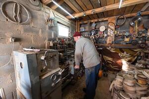 A senior man procesing wood on a lathe and making wooden dishes in the workshop photo