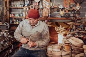 A senior man sitting in the workshop and processing wooden utensils in the old manual way photo