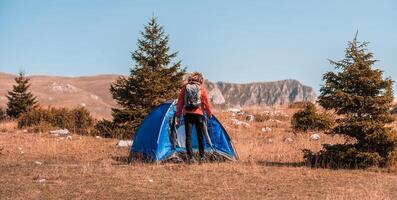 A man with a tent enjoys a sunny day whileusing a smartphone and camping in the mountains photo
