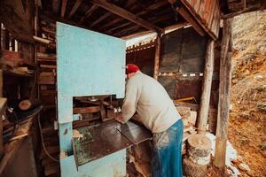 A senior man processing wood on a machine in an outdoor workshop. photo