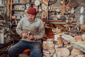 A senior man sitting in the workshop and processing wooden utensils in the old manual way photo