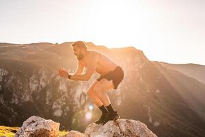 Man doing conditioning training on top of a mountain in the early morning with the sunrise in the background photo