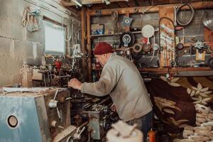 A senior man procesing wood on a lathe and making wooden dishes in the workshop photo