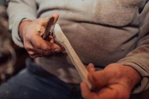 A senior man sitting in the workshop and processing wooden utensils in the old manual way photo