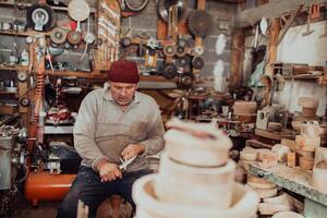 A senior man sitting in the workshop and processing wooden utensils in the old manual way photo