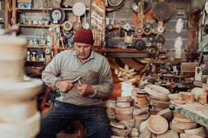 A senior man sitting in the workshop and processing wooden utensils in the old manual way photo