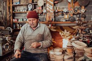 A senior man sitting in the workshop and processing wooden utensils in the old manual way photo