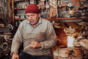 A senior man sitting in the workshop and processing wooden utensils in the old manual way photo