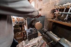 A senior man procesing wood on a lathe and making wooden dishes in the workshop photo