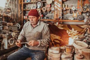 A senior man sitting in the workshop and processing wooden utensils in the old manual way photo