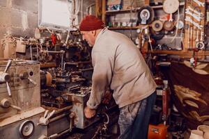 A senior man procesing wood on a lathe and making wooden dishes in the workshop photo