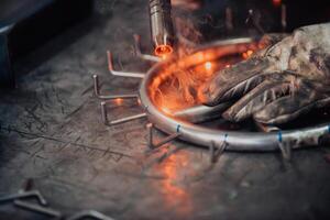 Close up welder in protective uniform and mask welding metal pipe on the industrial table with other workers behind in the industrial workshop. photo