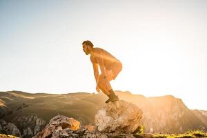 Man doing conditioning training on top of a mountain in the early morning with the sunrise in the background photo