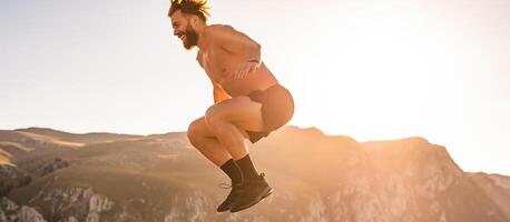 Man doing conditioning training on top of a mountain in the early morning with the sunrise in the background photo