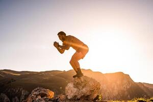 Man doing conditioning training on top of a mountain in the early morning with the sunrise in the background photo
