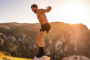 Man doing conditioning training on top of a mountain in the early morning with the sunrise in the background photo