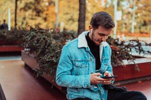 A gappy student sitting in a park using a smartphone and wireless headphones photo