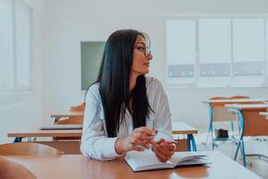 A black-haired female student wearing glasses is attentively engaged in a modern classroom, embracing education and learning with focus and curiosity photo