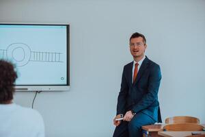 A modernly dressed professor engages in educating students, who listen attentively, creating a dynamic scene of knowledge-sharing and focused learning in the classroom. photo