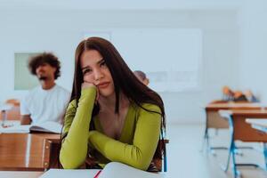 A weary-looking student sitting in front of a group of diverse students in a modern classroom, capturing the blend of exhaustion, learning, and collaboration in their academic journey photo
