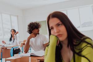 A weary-looking student sitting in front of a group of diverse students in a modern classroom, capturing the blend of exhaustion, learning, and collaboration in their academic journey photo