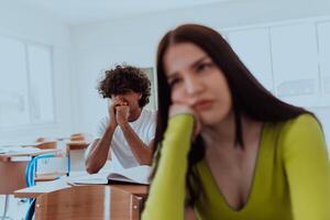 A weary-looking student sitting in front of a group of diverse students in a modern classroom, capturing the blend of exhaustion, learning, and collaboration in their academic journey photo