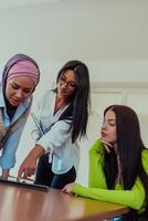 Group of business woman one of them is wearing a hijab, are reviewing papers and a laptop together, creating new business projects, demonstrating teamwork, collaboration, and productivity. photo