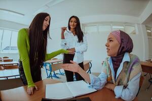 Group of business woman one of them is wearing a hijab, are reviewing papers and a laptop together, creating new business projects, demonstrating teamwork, collaboration, and productivity. photo