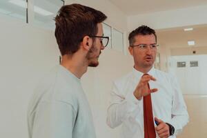 The director conducts a conversation with the secretary and a young programmer in a modern and spacious corridor of a large company, discussing various business topics and projects. photo