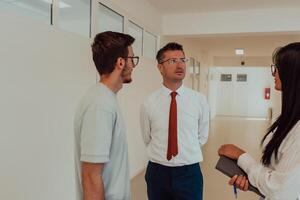 The director conducts a conversation with the secretary and a young programmer in a modern and spacious corridor of a large company, discussing various business topics and projects. photo