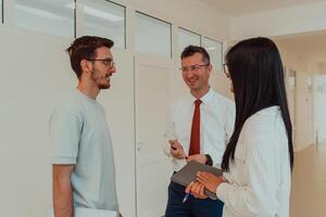 The director conducts a conversation with the secretary and a young programmer in a modern and spacious corridor of a large company, discussing various business topics and projects. photo