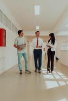 The director conducts a conversation with the secretary and a young programmer in a modern and spacious corridor of a large company, discussing various business topics and projects. photo