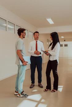 The director conducts a conversation with the secretary and a young programmer in a modern and spacious corridor of a large company, discussing various business topics and projects. photo