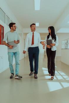 The director conducts a conversation with the secretary and a young programmer in a modern and spacious corridor of a large company, discussing various business topics and projects. photo