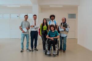 A group of students with a professor and a colleague who is in a wheelchair are standing together in the corridor of a modern university photo