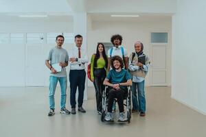 A group of students with a professor and a colleague who is in a wheelchair are standing together in the corridor of a modern university photo
