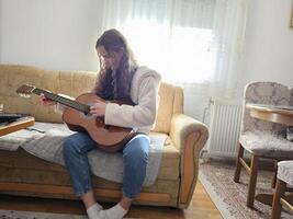 The young, curly-haired girl plays her acoustic guitar with passion and talent in the comfort of her home, creating beautiful melodies in this realistic photograph photo