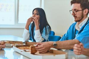 A group of doctors takes a well-deserved break in the hospital, savoring slices of pizza and sharing moments of camaraderie during their busy workday photo