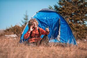 A man with a tent enjoys a sunny day whileusing a smartphone and camping in the mountains photo