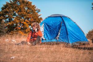 A man with a tent enjoys a sunny day whileusing a smartphone and camping in the mountains photo