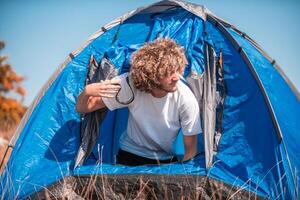 A man with a tent enjoys a sunny day whileusing a smartphone and camping in the mountains photo