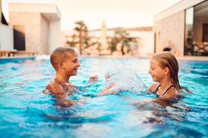 In a sunlit modern villa, a young brother and sister joyfully splash and play in the pool, basking in the warmth of a perfect summer day photo