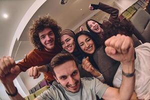 A diverse group of young people exuberantly celebrates and cheers while watching a soccer match, radiating excitement, unity, and sportsmanship photo