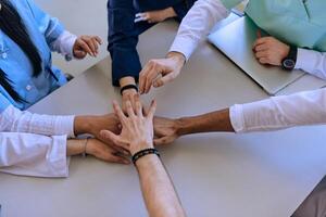 A group of doctors and a medical nurse join their hands together on a table, showcasing the unwavering teamwork and solidarity that drives their collective efforts in the healthcare field photo