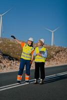 A engineer with a tablet and her colleague inspect wind turbines in a field, demonstrating teamwork and dedication to renewable energy projects photo
