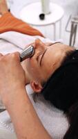 A woman massages her face using a gadget with microcurrents. video