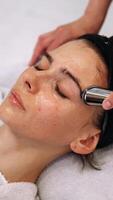 A woman massages her face using a gadget with microcurrents. video