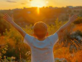 A young boy is standing in a field with his arms raised, smiling photo