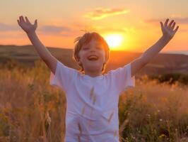 A young boy is standing in a field with his arms raised, smiling photo