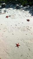 SUMMER written on the sand on a tropical beach with red starfish and shells. video